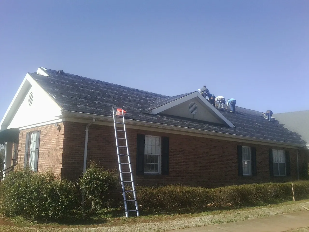 Crew tearing shingles off a brick ranch roof with a ladder set — Emergency Roof Repair work by our crew in Glenmoore