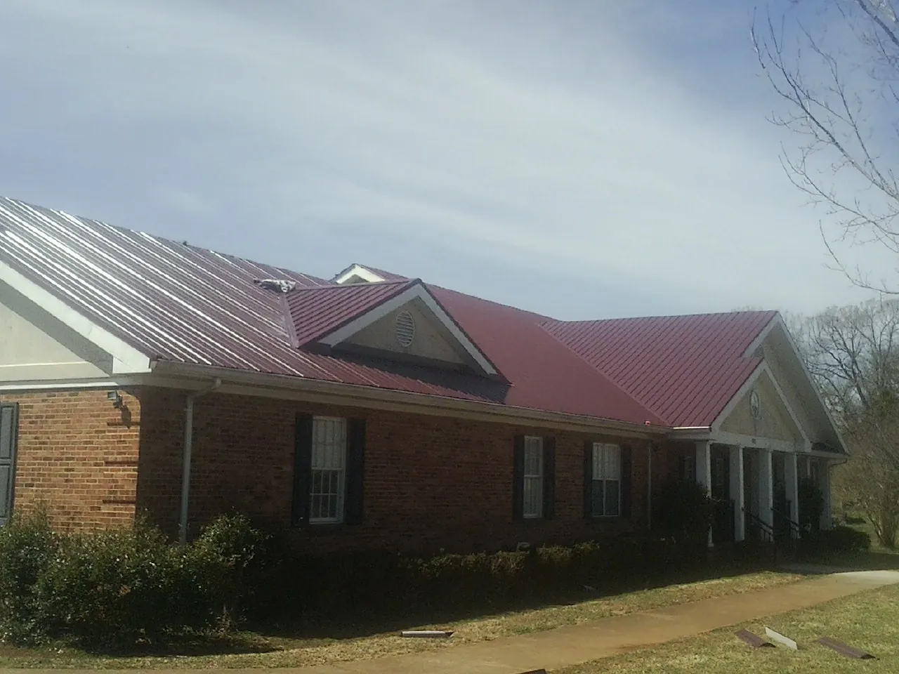 Red metal roof with gabled entries on a long brick building, from a Hail Damage Roof Repair job in Glenmoore