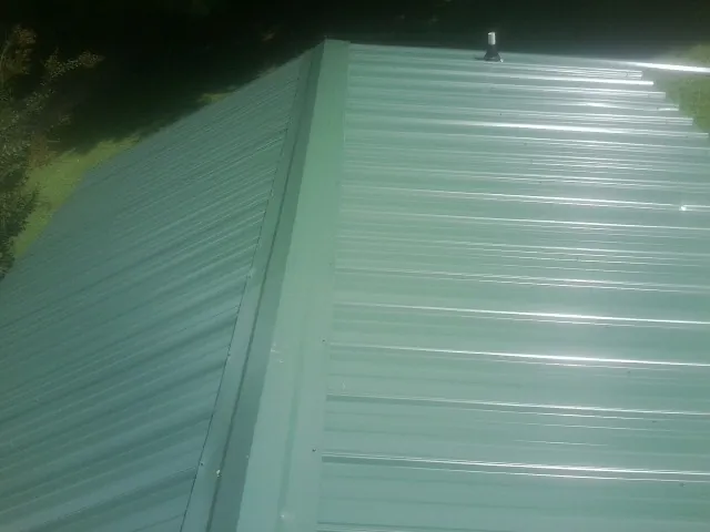 New green metal panels meeting at the ridge of a roof — Flat Roof Repair work by our crew in Glenmoore