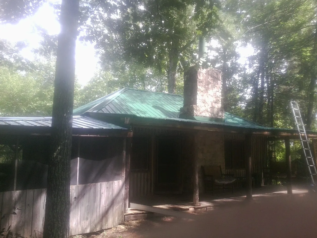 Green metal roof and stone chimney above a log cabin porch in Glenmoore