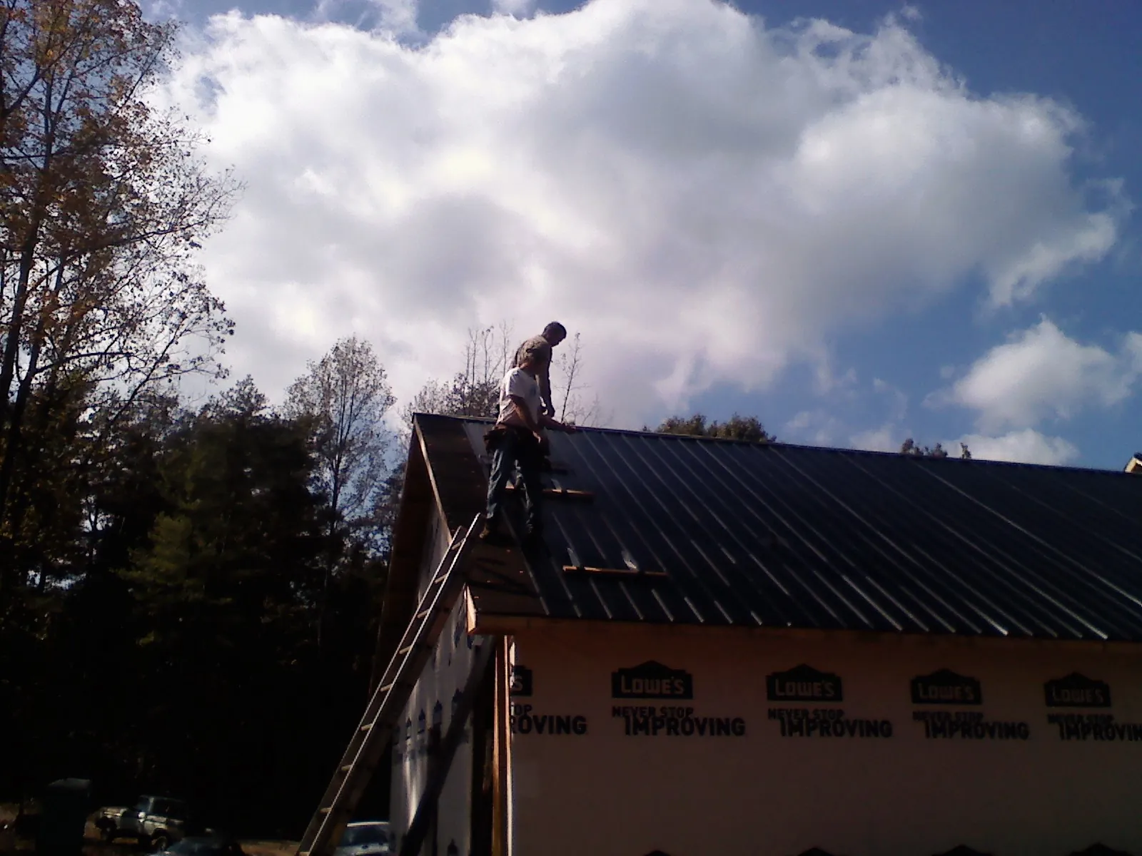 Roofer fastening dark metal panels high against a cloudy sky, from a Roof Inspection job in Glenmoore